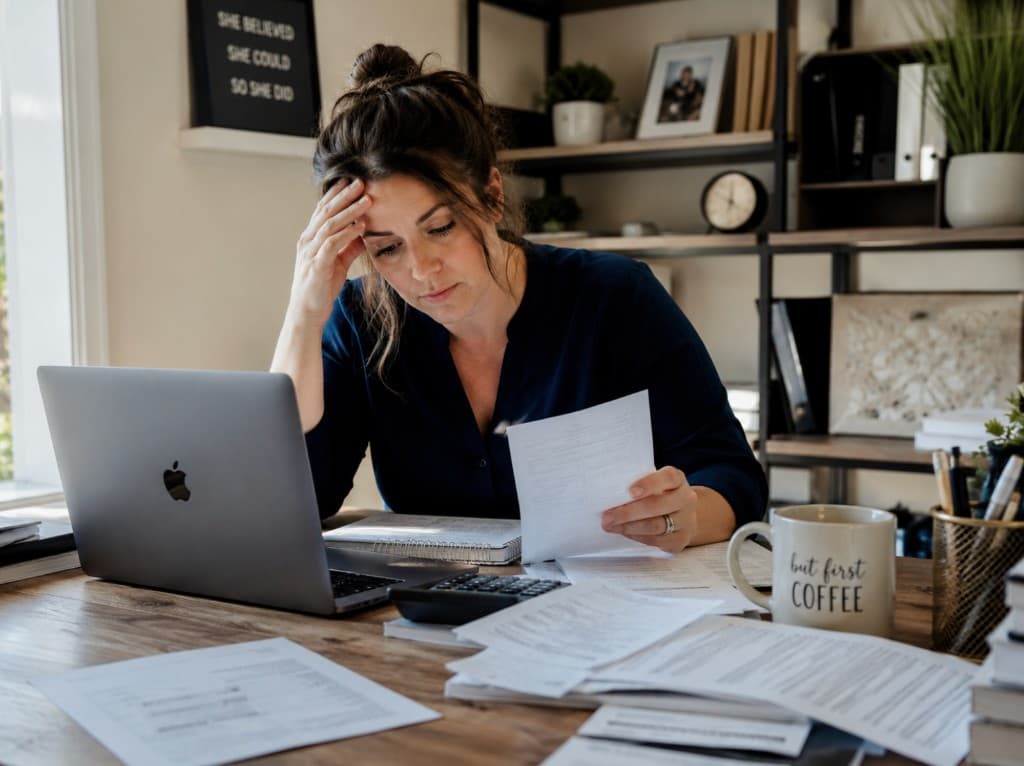 Business owner reviewing paperwork at a desk, looking stressed by bookkeeping